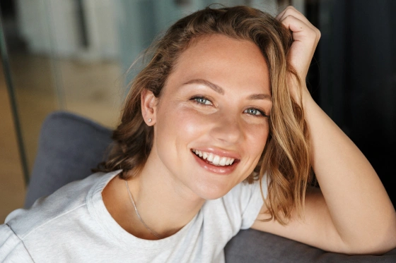 Smiling woman with reddish-brown hair in casual white shirt, relaxed indoor setting.