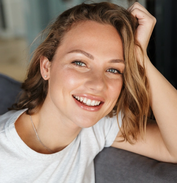 Smiling woman in white t-shirt with hand in hair, relaxed indoor portrait setting.