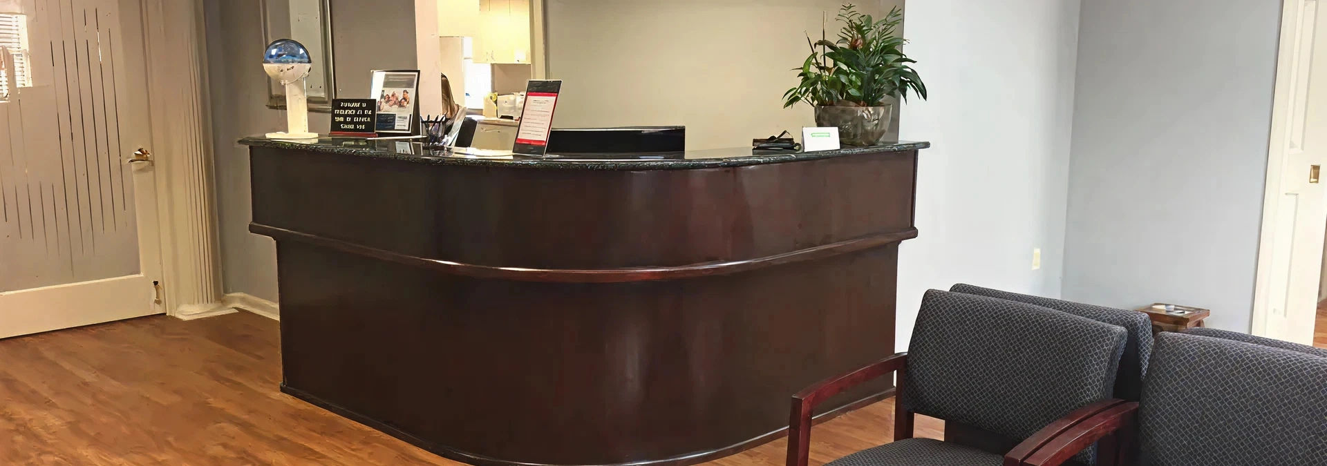 Modern dental office reception area with curved dark wood desk and waiting seating.