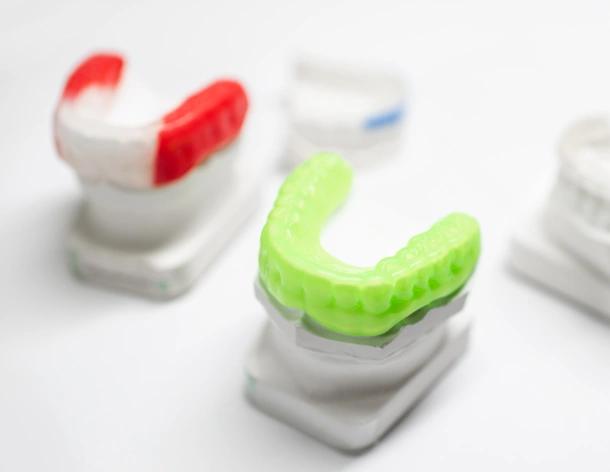Colorful dental mouthguards and retainers displayed on white pedestals in a dental office setting.