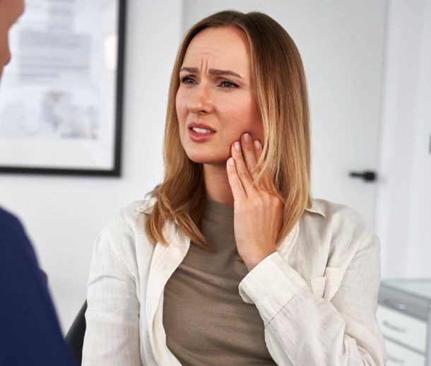 Woman in office setting holding face with concerned expression about dental issue.