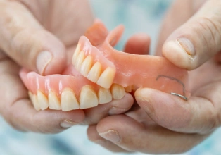Hands holding dentures or false teeth against blurred background for dental education.