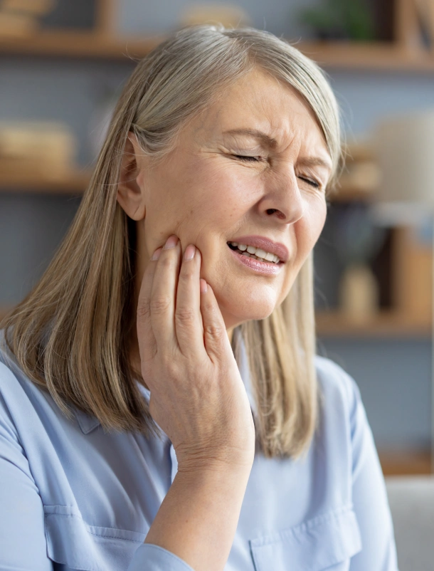 Woman experiencing tooth pain, holding her cheek, in a clinical dental office setting.