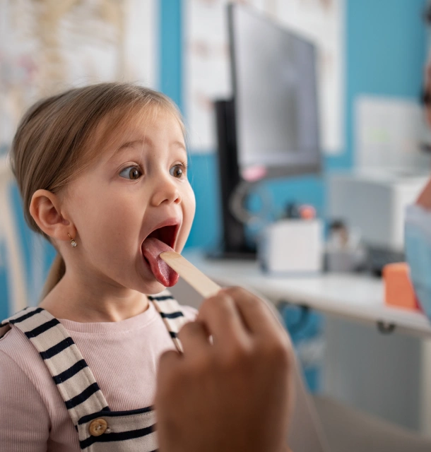 Young child having dental examination with tongue depressor in clinical dental office setting.
