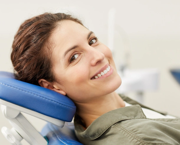 Smiling woman resting head on blue dental pillow in modern dental office setting.