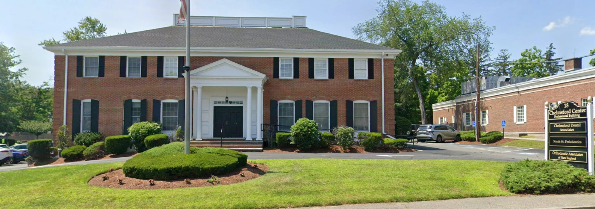 Brick colonial dental office building with manicured lawn and landscaping in residential setting.