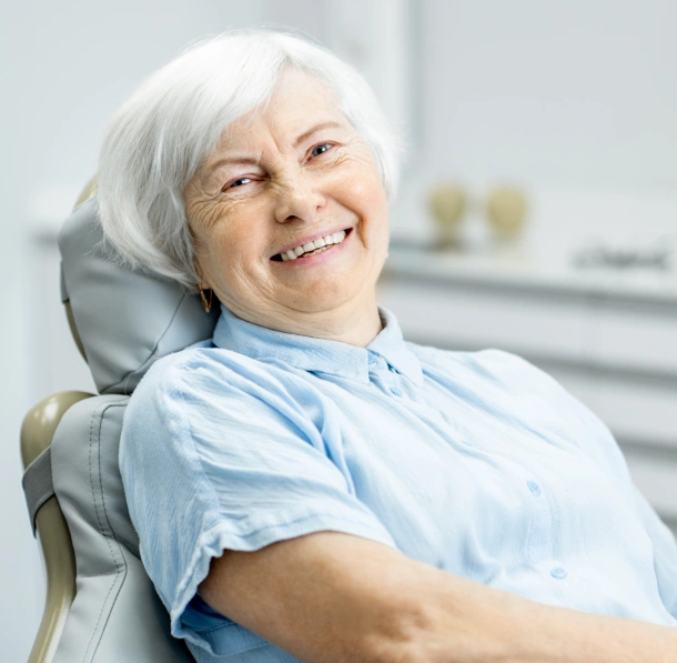 Smiling senior woman in light blue shirt sitting in dental chair at Chelmsford Dental Associates office.