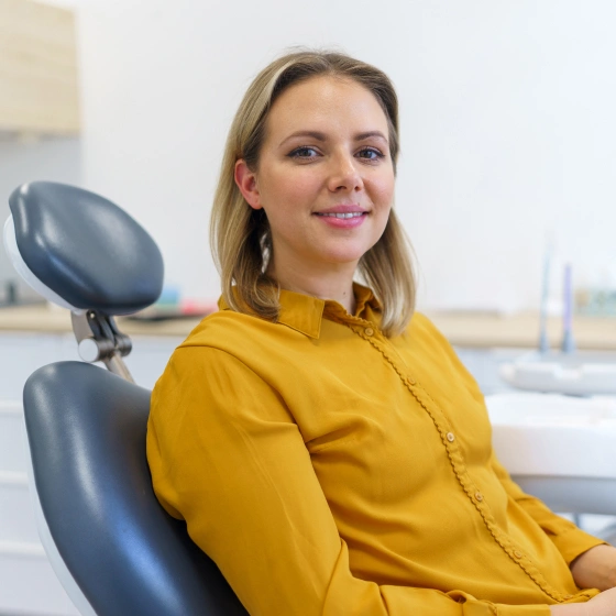 Woman in yellow shirt smiling in dental office chair with equipment visible in background.