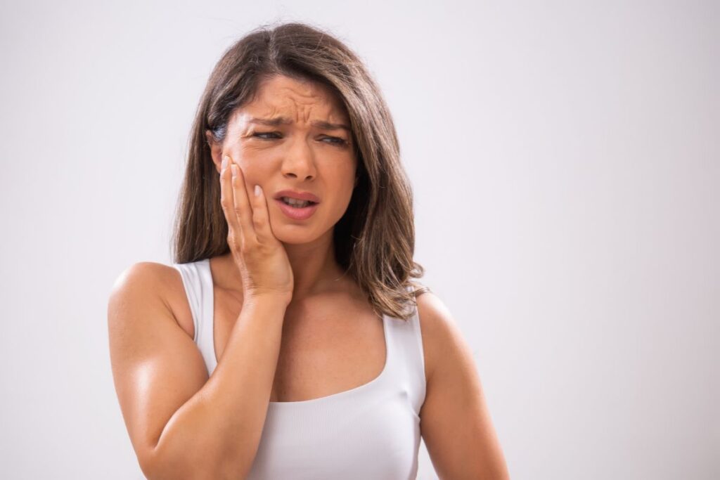 Woman holding her cheek in discomfort, showing signs of tooth pain or dental sensitivity.
