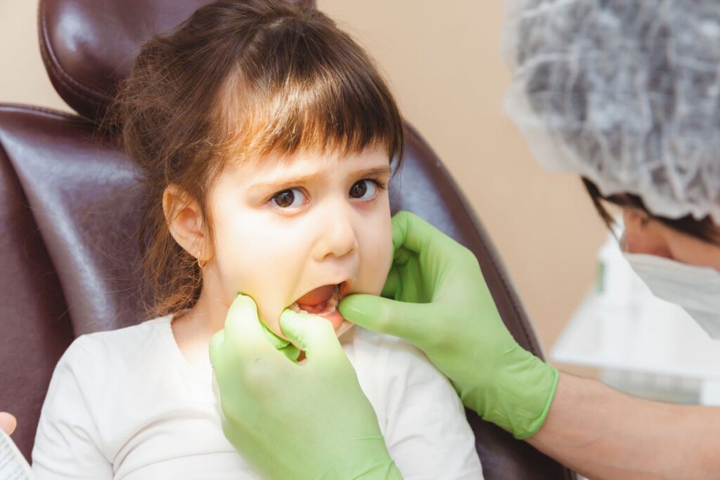 Young child undergoing a dental examination while a pediatric dentist checks their teeth and gums during a routine dental visit.