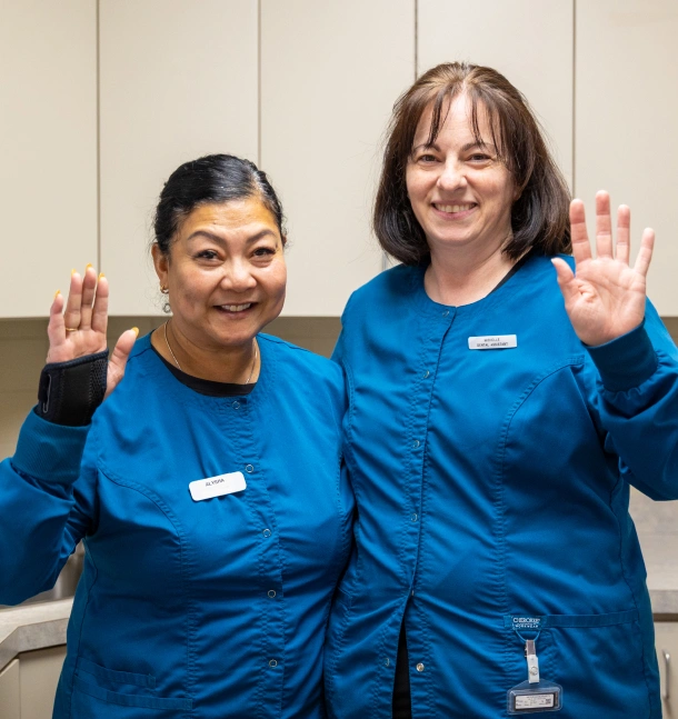 Two dental team members in blue scrubs waving and smiling