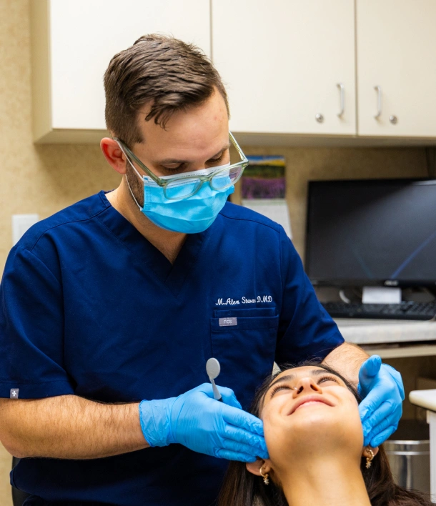 Dentist in mask and gloves examining a smiling patient's teeth