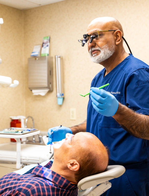 Dentist in scrubs and loupes treating a patient in the dental chair