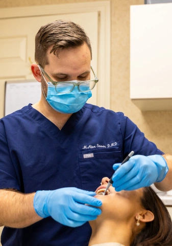 Dentist in mask and gloves examining a patient's teeth during a dental cleaning