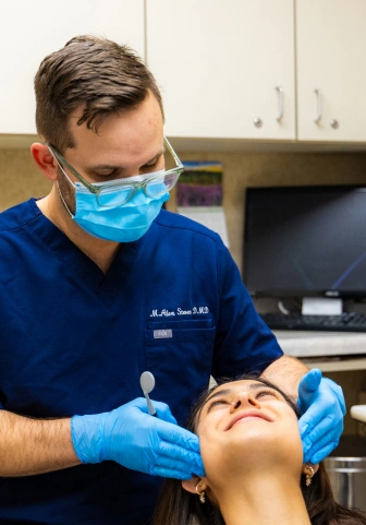 Dentist in mask and gloves treating a smiling patient in a dental chair
