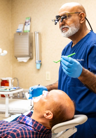 Dentist in scrubs and magnifying loupes performing a procedure on a patient in the dental chair