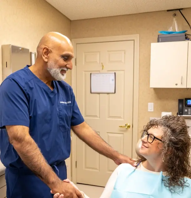 Dentist in blue scrubs shaking hands with female patient in dental office.