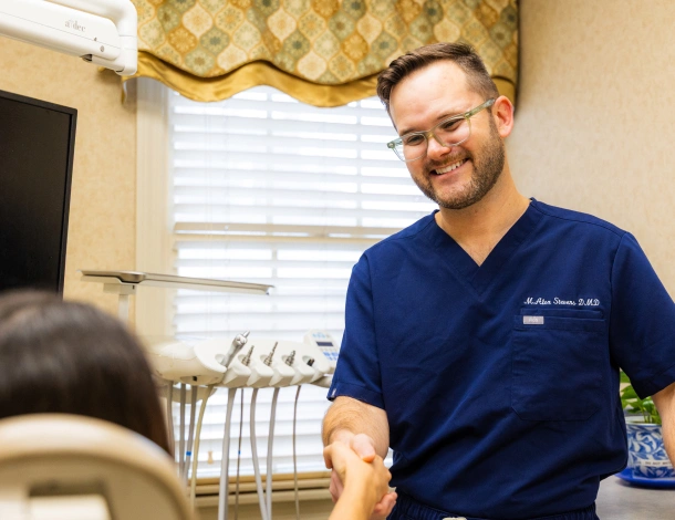Dentist in scrubs smiling and shaking hands with a patient