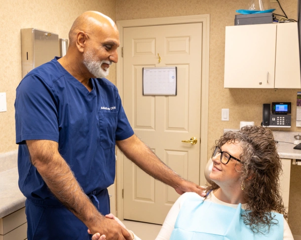 Dentist in scrubs smiling with a patient in the dental chair